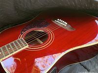 Close-up of the body of the acoustic guitar showing reddish finish, tortoiseshell style pickguard, and white bridge pins, highlighting the condition and color.