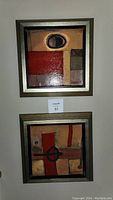 Two framed square paintings stacked vertically on wall