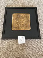 Frontal view of the framed bronze engraving showing the entire 17x17 inch black matte frame and bronze artwork centered.