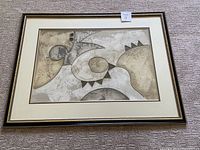 Full view of framed abstract artwork by Kennedy, showing neutral toned abstract shapes and black and gold frame with cream mats.