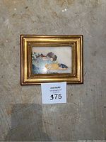 Photo of framed stone mosaic art lying on floor, showing gold multi-layered wooden frame and artwork inside.