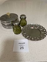 Photo of the full lot showing the metal and glass candy dish, green glass salt and pepper shakers, and decorative metal plate on a white surface
