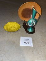Photo showing yellow ceramic shell dish, wooden bowl, and green decorative pitcher with wooden stand placed on the floor.