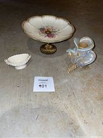 All three items displayed together on concrete floor: floral pedestal dish, small white jewelry dish, opalescent flower candle holder