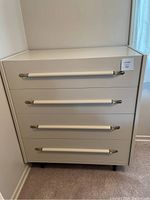 Front view of a four drawer white wooden dresser with metal accented handles