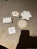 Three jewelry dishes displayed: two fine China dishes with floral patterns and gold trim, and one white ruffled glass dish