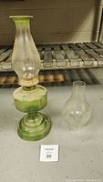 Image of the green glass oil lamp with the attached chimney and the extra clear glass chimney beside it, showing overall items and condition.