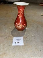 Full view of tall Rosenthal vase with flower design on a red base, gold trim on the rim, photographed on a concrete floor.