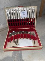 Silverware set in open box showing knives secured at top and other utensils in right slots with red velvet and cream lining.
