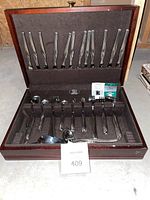 Full silverware set in open wooden box showing knives, forks, spoons, and serving pieces.