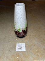 Tall glass vase with white, green, and purple colors on a concrete floor.