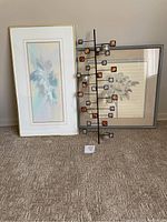 Three items together: tall framed abstract pastel art on left, metal candle holder wall decor in middle, framed flower print on right.