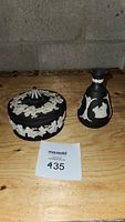 Both Wedgwood black jasperware decorative covered dish with lid and vase displayed on a wooden surface.