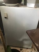 Exterior front view of white miniature refrigerator showing door with handle.