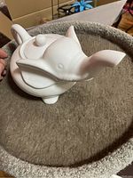 White ceramic elephant-shaped teapot, side view with trunk spout visible, set on beige carpeted surface.