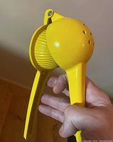 Handheld yellow metal citrus juice press held in hand to show size and details