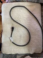 Top view of the white plush cover with the black and white power cord coiled on top, showing fabric texture and cord plug