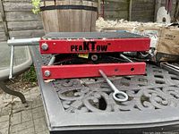 Side view of red steel PEAKTOW motorcycle jack in closed position, showing robust scissor lift frame and lifting platform.