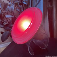 Photo of the multicoloured programmable lamp emitting red light on a clear curved base.