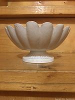 Side view of white scalloped footed bowl showing overall shape and elevation on pedestal base.