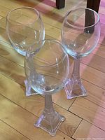 Photo showing three clear wine glasses with bases modeled after the Eiffel Tower, placed on a wooden floor.