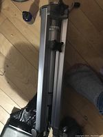 Folded aluminum tripod legs with locking knobs on wooden floor.