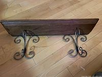 Side view of the wall-mounted wooden plate rack with wrought iron brackets showing decorative scroll work and shelf depth.