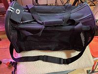 Side view showing black nylon material with mesh ventilation panel, double carry handles, and shoulder strap with padding.