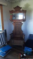 Front view of oak hall tree showing carved crest, mirror, bench seat and coat hooks