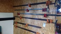 Seven bar clamps mounted on a wood panel wall, showing varying sizes and colored clamping jaws mainly orange and some red.