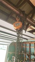 Block and tackle hoist hanging from an overhead beam in a barn. Visible heavy chain and 1 ton capacity label on hoist.