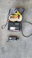 Motomaster battery charger with attached power cord and carrying case with booster cables on floor