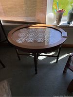 Round wooden display table with removable glass top, showing the table positioned near a window with light filtering through.