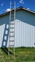 Full view of the aluminum extension ladder set upright against a white barn wall showing its height and structure