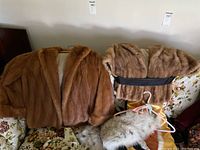 Two fur coats displayed on a floral couch with a fur collar and zip-up storage cover, showing their styles and colors.