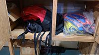 Two large backpacks on a wooden shelf, one red and black, the other dark colored and waterproof