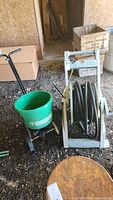 Photo showing hose reel with hose wound and seed spreader in background in barn/shed