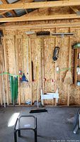 Photo of rakes, push broom, hand broom, squeegee, and other hanging garden tools on a wooden wall.
