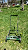 Front view showing green mower body, black handle, and front reel mechanism.
