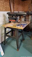 Side view of the Craftsman radial arm saw mounted on metal stand with extra blades and manuals on the surface.