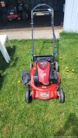 Front-facing view of red Toro lawn mower on grass, showing cutting deck and attached grass bag.