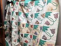 Full view of the folded quilt hanging to show overall design with appliqued flowers and scalloped edges.