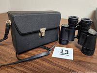 Black carrying case with shoulder strap closed beside Sears binoculars.