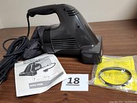 Side view of Black & Decker Dirt Vac handheld vacuum with instruction manual and extra belt pouch laid beside it on table.