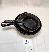 Stacked view of four cast iron skillets showing size comparison and condition of handles and cooking surfaces.