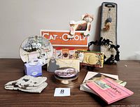 Photo showing full collection of cat-themed items including Cat-Opoly game box, figurines, plate, scratching pad, wall hangings, socks, tin, and books
