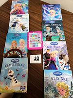 Overview of eight hardcover books themed around Disney's Frozen and Disney Princesses with a pink LeapFrog Tag electronic reading device in the middle on a wooden surface.