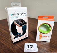 Photo showing Fitbit Versa 2 smartwatch box and separate smart bracelet box on a table with lot number 12.