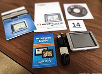 Garmin Nuvi GPS device with USB cable and multiple user guides and a CD disk arranged on a wooden surface.