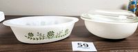 Both Glasbake oval milk glass casserole with green design and Pyrex round opal white casserole with glass lid shown side by side
